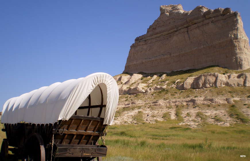 A covered wagon on the grassland below Scotts Bluff