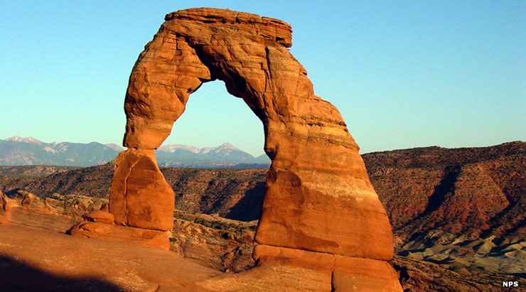 Delicate Arch with a canyon wall and distant mountains in the background