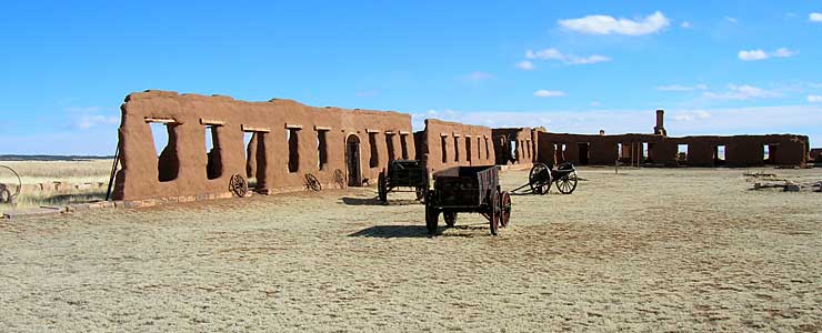 Freight wagons and a cannon stands in front of adobe walls at Fort Union National Monument